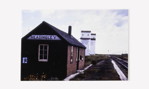 Headingley Railway Station and Coop Elevator train stopped for passengers, mail, grain, flour, and milk shipment to Winnipeg. Moved July 1994